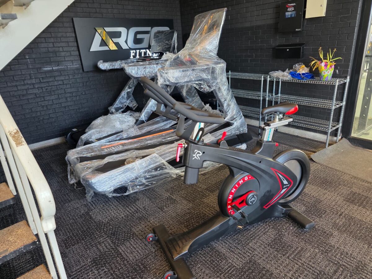 ARGO Fitness   Gym showroom with a wrapped treadmill and a front facing exercise bike in the foreground against a dark brick wall