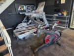 ARGO Fitness   Gym showroom with a wrapped treadmill and a front facing exercise bike in the foreground against a dark brick wall