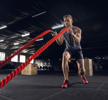 Young healthy male athlete doing exercises in the gym Young healthy man, athlete doing exercise with the ropes in gym. Single male model practicing hard and training his upper body. Concept of healthy lifestyle, sport, fitness, bodybuilding, wellbeing.