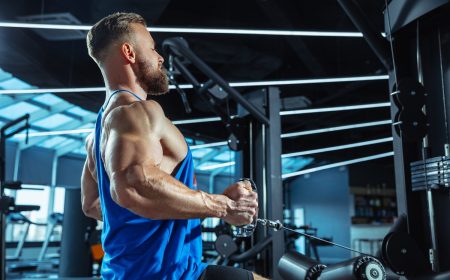 The male athlete training hard in the gym. Fitness and healthy life concept. Young muscular caucasian athlete training in gym, doing strength exercises, practicing, work on his upper body, pulling on weights and barbells. Fitness, wellness, healthy lifestyle concept, working.
